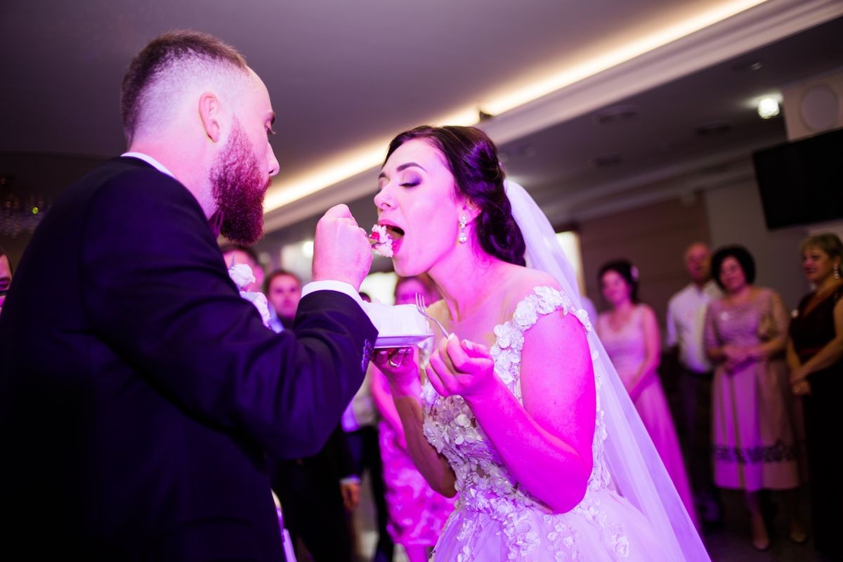 The groom feeds her bride with a piece of cake at a wedding party